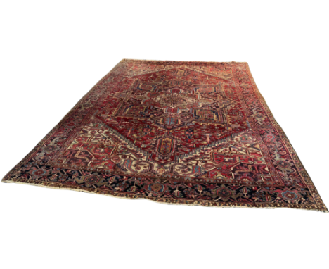 A Heriz Persian carpet, the madder red ground bearing a large central floral medallion, ivory spandrels and main geometric fl
