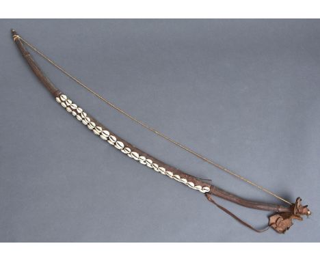 Tribal art. A wood, leather and fibre archer's bow applied with three strings of cowrie shells, early 20th c, 99cm l  Leather