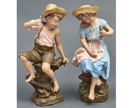 A pair of Goldscheider cold painted terracotta figures of a barefoot boy and girl, 1897-1914, seated on rocks with a fish, 43