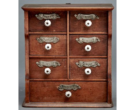 Kitchenalia. A light wood spice cabinet, early 20th c, of seven drawers with embossed tin label and white glass daisy knop, 2