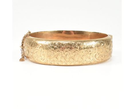 A hallmarked 9ct gold hinged bangle. The gold bangle having bright cut engraved floral decoration to plain verso, complete wi