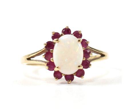 A hallmarked 9ct gold, opal and ruby cluster ring. The ring having a central opal cabochon surrounded by a halo of twelve rou