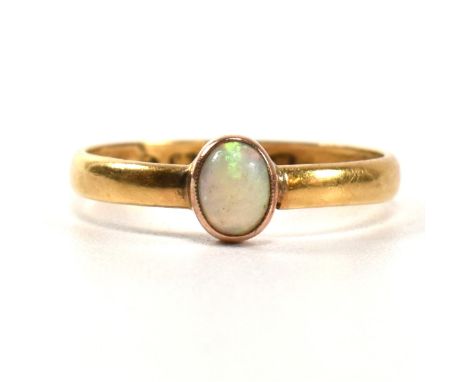 A Victorian hallmarked 22ct gold and opal ring. The ring having a single oval cut opal cabochon with millegrain border to pla