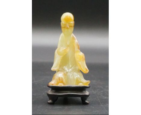 A Chinese carved mottled green jade seated figure, 8.7cm high,&nbsp;on fitted hardwood stand.&nbsp; 