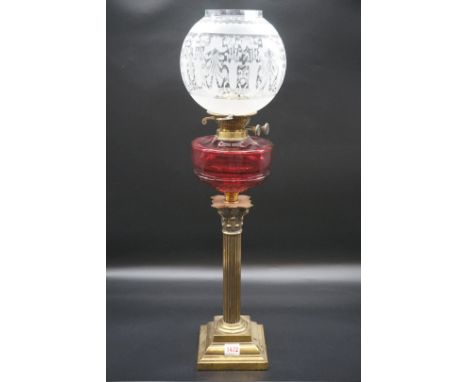 An antique brass Corinthian column oil lamp,&nbsp;with ruby glass reservoir and etched shade, height including shade 70cm, (c