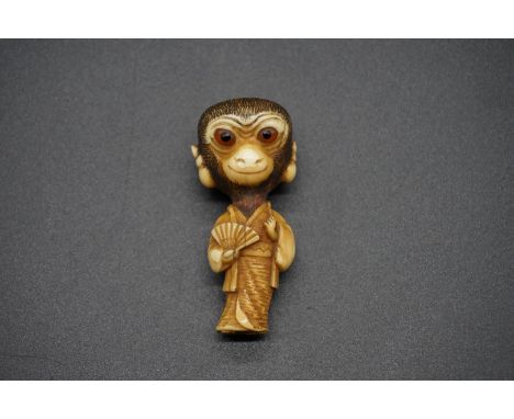 An unusual Japanese carved ivory netsuke, Meiji, depicting a standing monkey in robes, with inset eyes, 5.4cm high. 