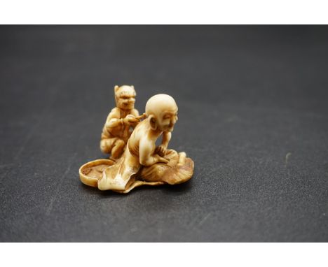 A good and unusual Japanese carved ivory netsuke, Edo, depicting a seated man receiving treatment from a small demon, 4cm wid