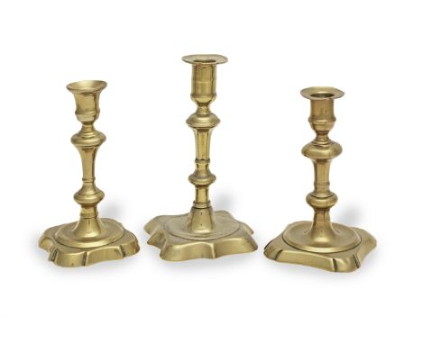 Three George II brass alloy socket candlesticks, circa 1730-55Two with bases with convex corners and concave sides, the third
