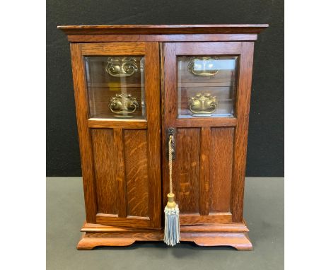 An Edwardian oak smokers cabinet, two door front enclosing fitted interior with four drawers above three pigeon holes, base s