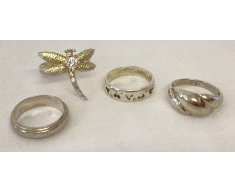 4 silver and white metal dress rings. Comprising: band ring, a dragonfly ring set with a clear stone, a band ring with pierce