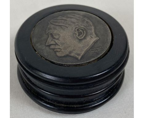 A German WWII style circular wooden snuff pot with cast metal plates inset to top and bottom. The top features a portrait in 