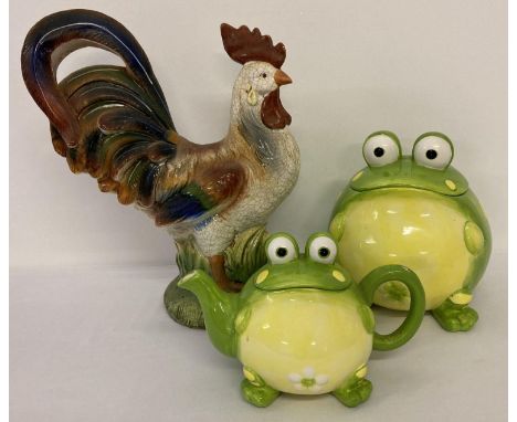 A large painted ceramic cockerel figurine together with a modern ceramic biscuit barrel and teapot in the form of frogs. 