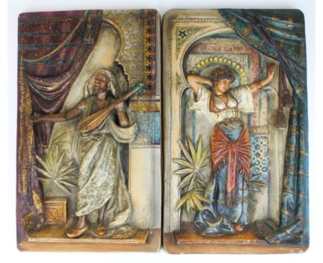 Two wall decorations with an Orientalist theme. They are made of terra cotta and painted. One shows a man playing a lute. The