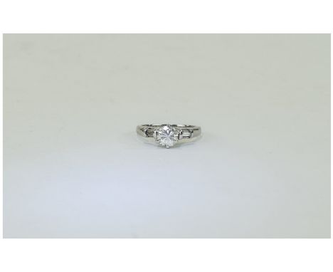 18 Carat White Gold Single Stone Diamond Ring set with a round brilliant cut diamond between baguette cut shoulders. Est diam