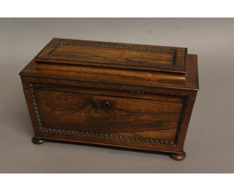 A REGENCY ROSEWOOD TEA CADDY, of sarcophagus form, the interior with twin lidded canisters and glass mixing bowl, on bun feet