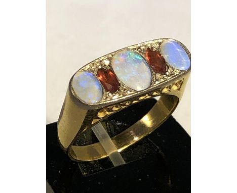 An opal and garnet ring, composed of three oval opals interspersed by two marquise garnets on a flat white metal grain ground