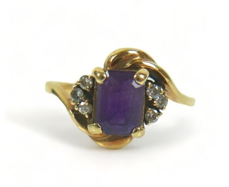 A yellow metal dress ring, set with a rectangular faceted cut purple stone, 7 by 5 by 3mm, flanked by six small diamonds, in 