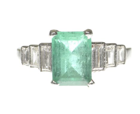 An Art Deco emerald and diamond ringCentering a step-cut emerald to graduated baguette-cut diamond shoulders, modelled in pre