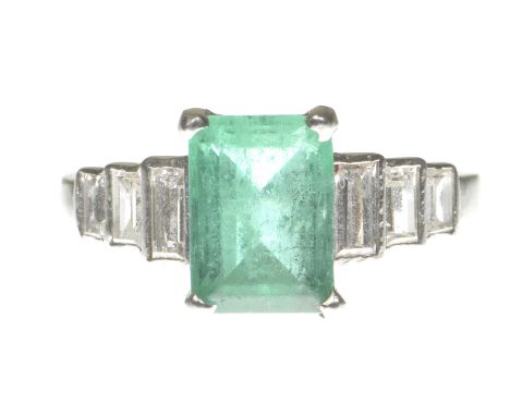 An Art Deco emerald and diamond ringCentering a step-cut emerald to graduated baguette-cut diamond shoulders, modelled in pre