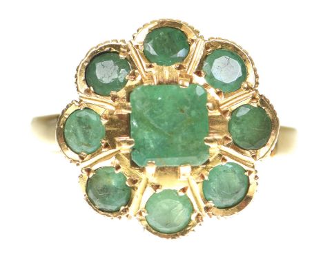 An emerald cluster ringCentering a step-cut emerald within a circular shape emerald surround, with an open work acanthus leaf