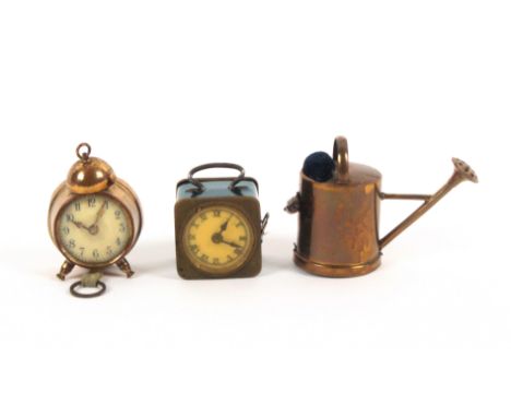 Three metal novelty tape measures, comprising a gilt brass watering can with velvet pin cushion, the printed tape in ins. and