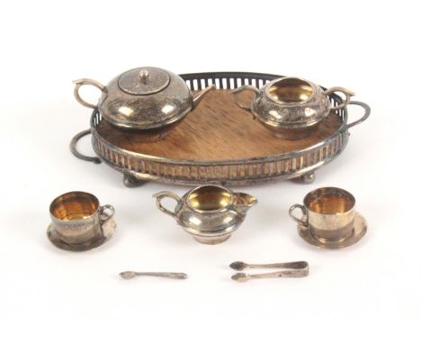 A miniature silver tea set, tray and accessories, the oak based oval tray on ball feet, 10cms, one handle detached but presen