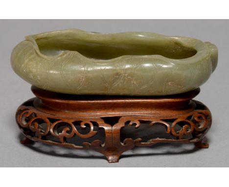 A CHINESE CELADON JADE BRUSH WASHER, 20TH C, CARVED AS A LOTUS, 12.5CM L, WOOD STAND (2) Tiny flea bites on everted rim of th