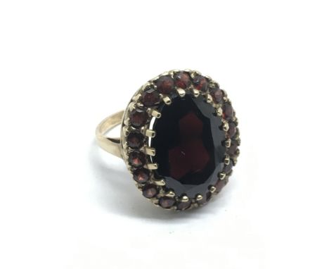 A gold ring set with a large garnet surrounded by smaller examples, approx 10.4g and approx size P.