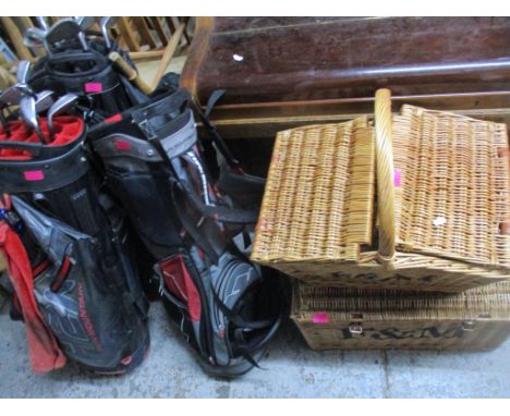 A group of three golf bags containing 13 iron golf clubs, two wicker hampers, and a vintage cloth and wooden bound trunk Loca