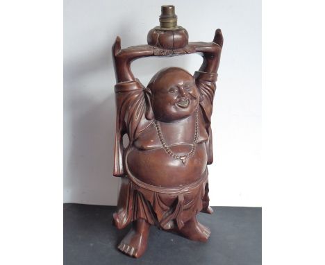 A early 20th century carved Chinese hardwood lamp modelled as a standing bald corpulent figure holding aloft a lotus flower (