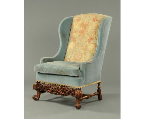 A walnut wing armchair, in the Carolean style, with woolwork tapestry back, loose cushion and with heavily carved front rail,