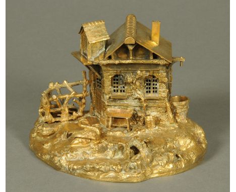 A gilt metal desk stand, with various apertures for inkwell, pens, etc., and in the form of a house by stream.  Height 17 cm,