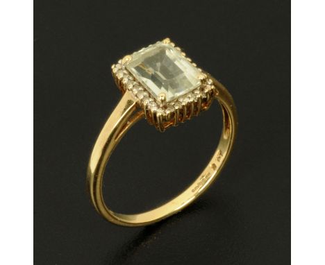 A gold and aquamarine ring, the central emerald cut gemstone in a surround of round cut diamonds. 