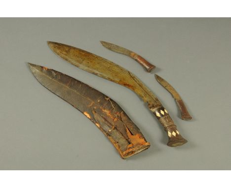 A Kukri knife, in scabbard, and two smaller knives.  Length 56 cm.  CONDITION REPORT: There is one piece of bone inlay missin