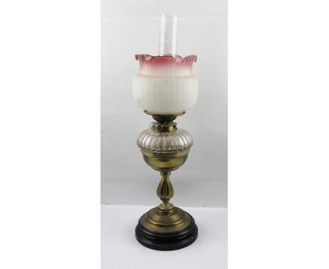 A LATE VICTORIAN OIL LAMP having brass stem, fitted with a clear glass reservoir and a pink tinted rimmed shade, overall 52cm