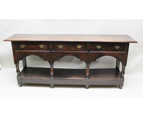 AN 18TH CENTURY OAK DRESSER BASE, having twin plank top over frieze, fitted three drawers with shaped back plate brass handle