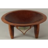 A VERY LARGE FIJIAN KAVA CARVED HARDWOOD BOWL, raised on four legs, with mounted metal plaque