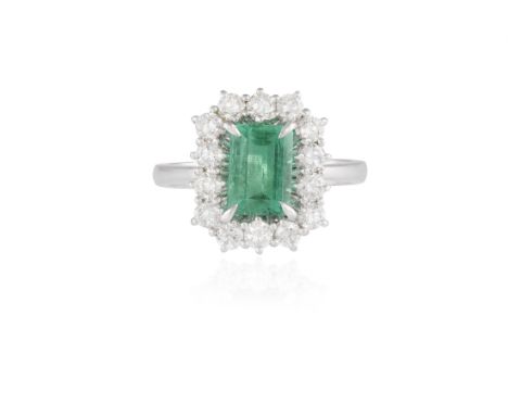 AN EMERALD AND DIAMOND CLUSTER RINGComposed of a central rectangular-cut emerald within a four-claw setting, surrounded by br