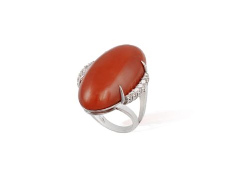 A CORAL AND DIAMOND COCKTAIL RINGThe large oval-shaped corallium rubrum coral cabochon within a four-claw setting, between br