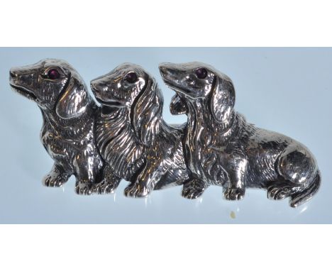 A stamped sterling silver brooch in the form of three Dachshunds set with ruby eyes. Weight 10g. Measures 4cm wide.