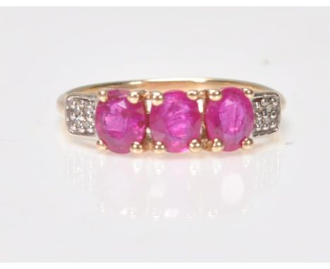 A 9ct gold ruby 3 stone ring. Stamped 375 with additional 10k mark. The 3 rubies within prong settings having illusion set sh