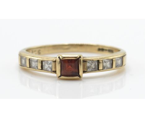 A 9ct gold ruby and diamond ring. The ring with cushion cut ruby flanked by inset diamonds to the shoulders on tapering shank