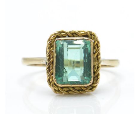 A 9ct gold and emerald ring. The ring set with a facet cut emerald in mount with rope twist border set to a plain shank. Tota