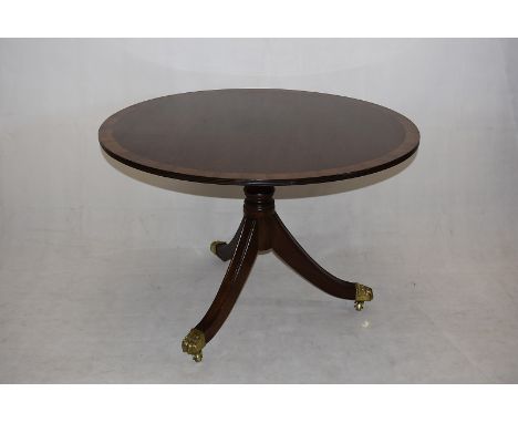A mahogany and satinwood hall table, having circular top, on tripod base, with brass paw casters, 107cm diameter x 74cm high