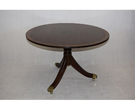 A mahogany and satinwood hall table, having circular top, on tripod base, with brass paw casters, 107cm diameter x 74cm high