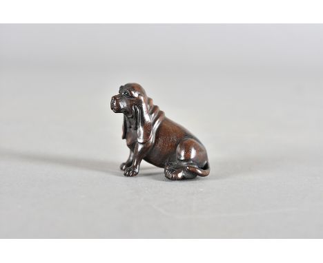 A Japanese hardwood netsuke, carved as a long eared spaniel with black glass eyes, 5 cm