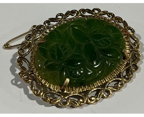 A 9ct gold mounted carved jadeite oval brooch, the green panel with leafy flower heads, openwork scroll mount marked 375, saf