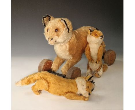 A vintage Steiff toy fox on wooden wheels, with button to one ear, 38cm long; and two smaller Steiff foxes, both with ear but