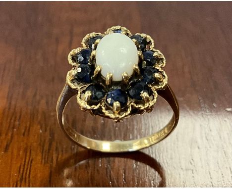 An opal and sapphire cluster ring, white oval opal cabochon surrounded by ten blue sapphires, 9ct gold shank, London 1975, si