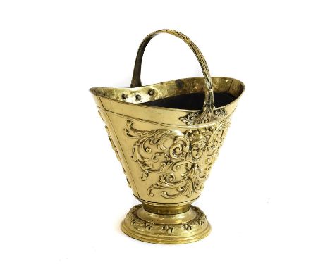 A Victorian Brass Coal Helmet, of flared oval form with overhead handle, repousse with masks and scrolling foliage, on circul